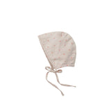 A light beige cotton bonnet with a small orange floral pattern and adjustable drawstrings, shown flat on a light gray background.